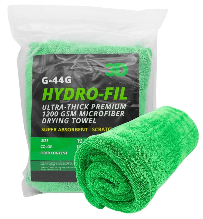 A rolled-up green microfiber drying towel is placed next to a transparent packaging sleeve. The package displays product information for the "3D Hydro-Fil Ultra-Thick Premium 1200 GSM Microfiber Drying Towel."