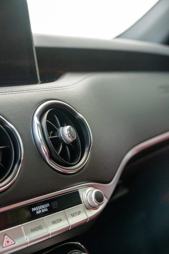 Close-up of a car's dashboard, featuring a silver air vent and digital control panel. The control panel includes buttons for radio, media, and setup, along with an indicator for the passenger airbag. The background is a blurred interior view.