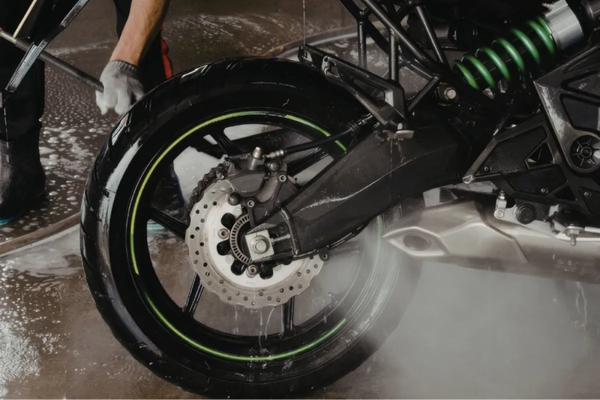 Detailer pressure washing a motorcycle rear wheel.