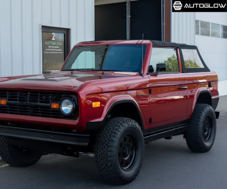 Front three-quarter view of a vintage dark red Ford Bronco with off-road tires parked outside a detailing garage.